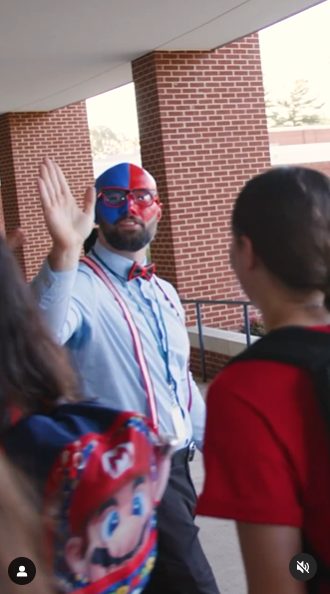 A teacher in red and blue facepaint high-fives a student