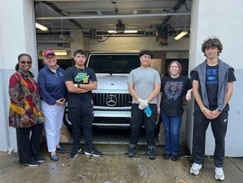 Group of students standing in front of a car in a garage.