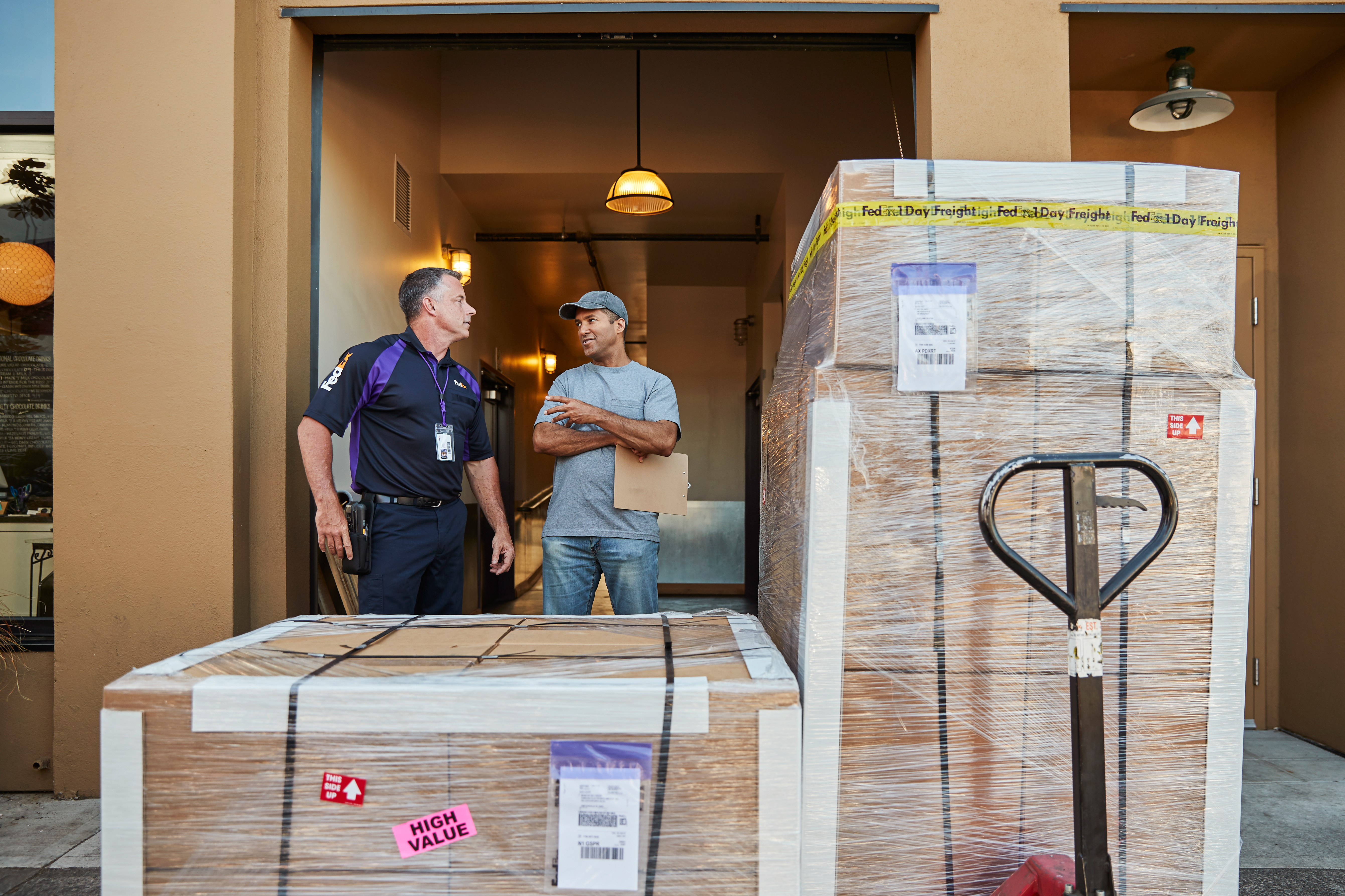 FedEx courier talking to a customer by some pallets