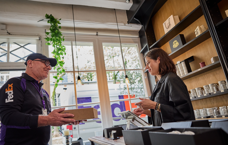 Smiling FedEx courier handing a package to a shop owner