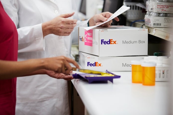 Pharmacy workers sort yellow pills on counter near FedEx boxes