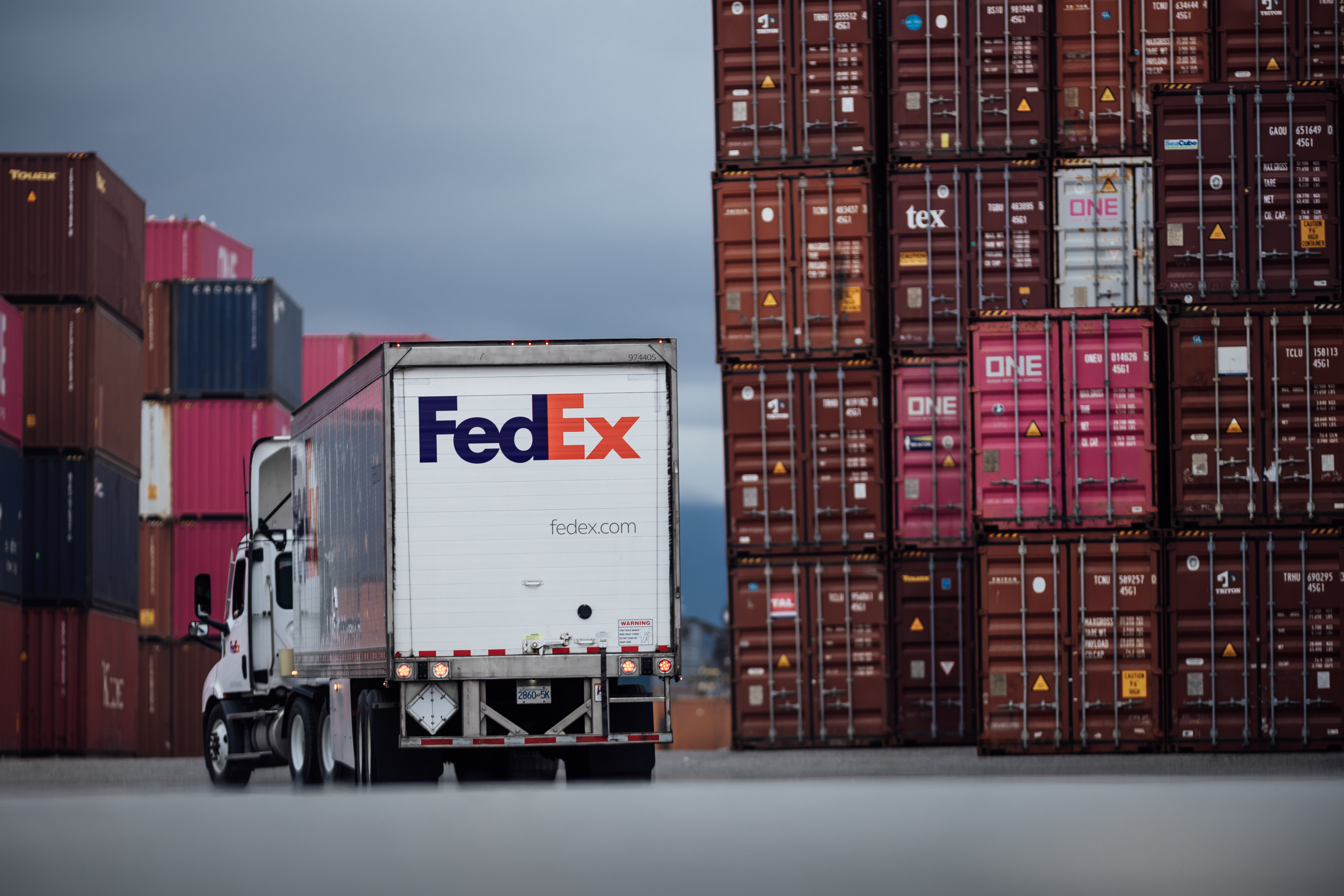 FedEx truck next to many stacks of shipping containers