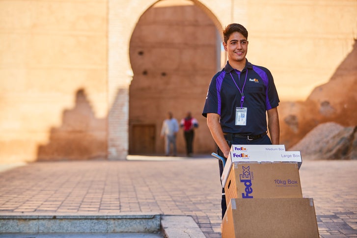 Smiling FedEx courier with a dolly of FedEx boxes