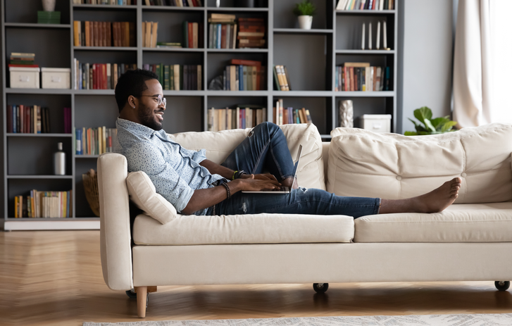 Lächelnde Person auf der Couch mit Laptop auf dem Schoß