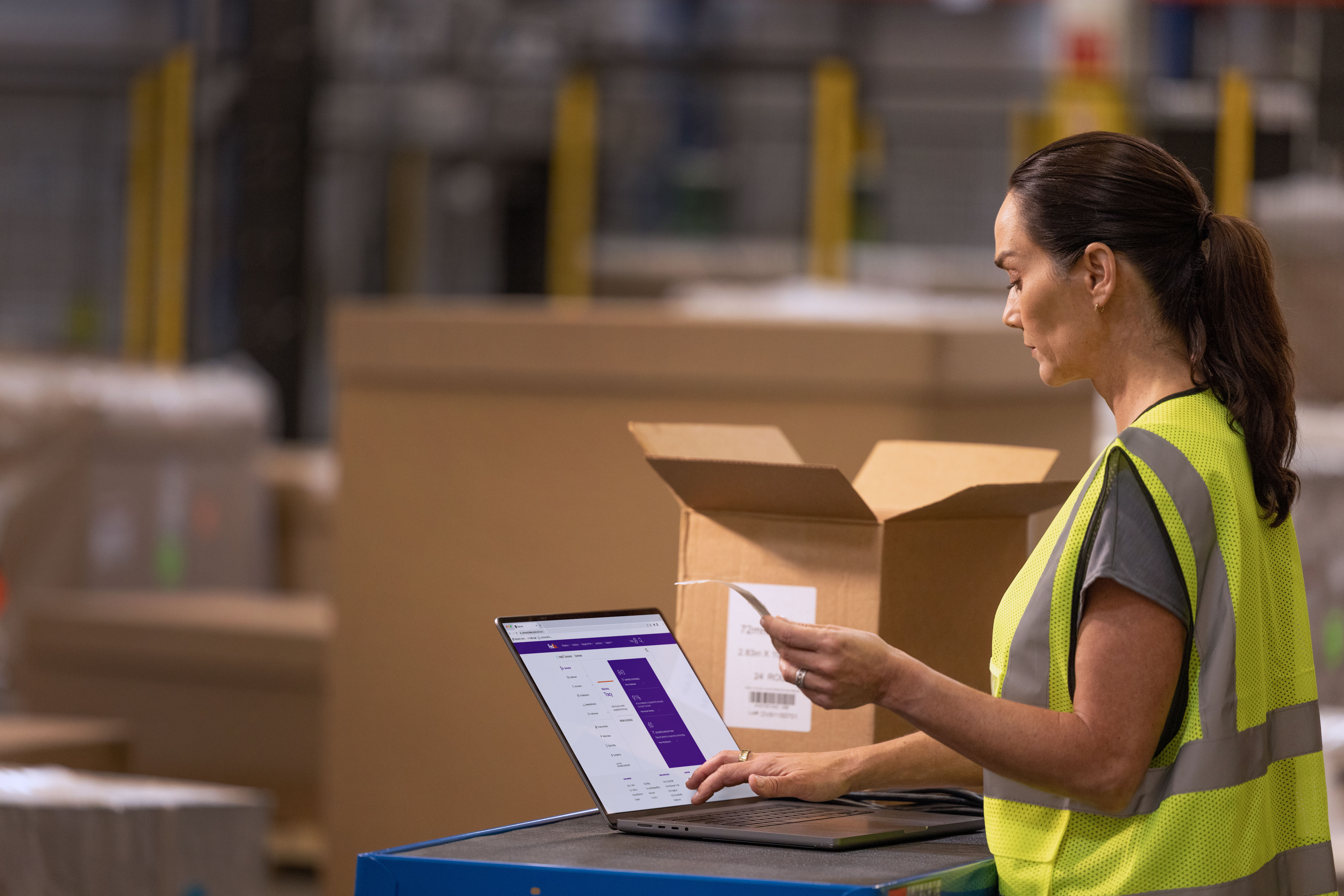 A warehouse worker entering in payment details while standing at a cart with a laptop and box on top.