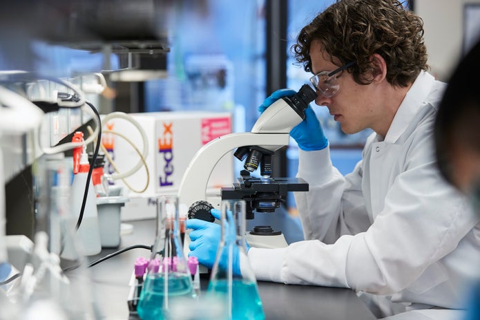 A lab technician looks into a microscope