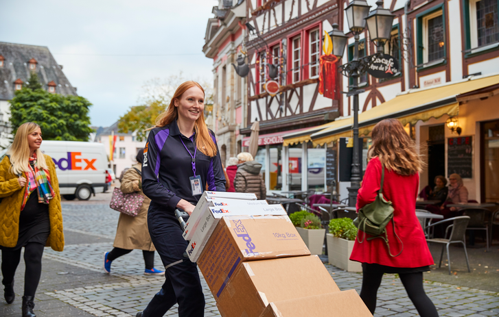 Lächelnde FedEx Kurierin mit Transportwagen