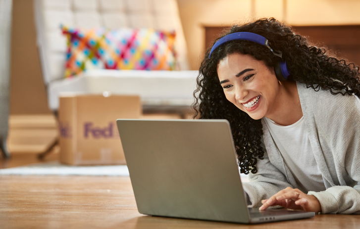 Lächelnde Person, die auf einen Laptop blickt, im Hintergrund steht eine braune FedEx Box