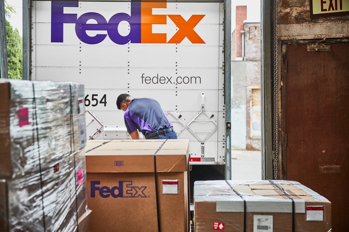 A courier standing at a loading dock locks the rear door of a FedEx Freight trailer