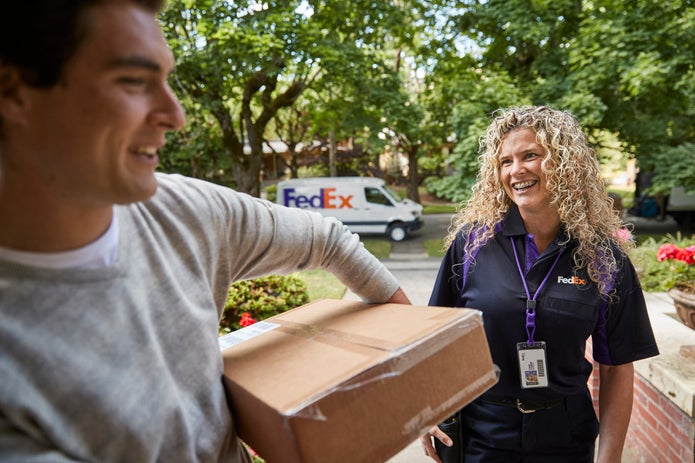 Comprador recibiendo un paquete de un conductor sonriente de FedEx