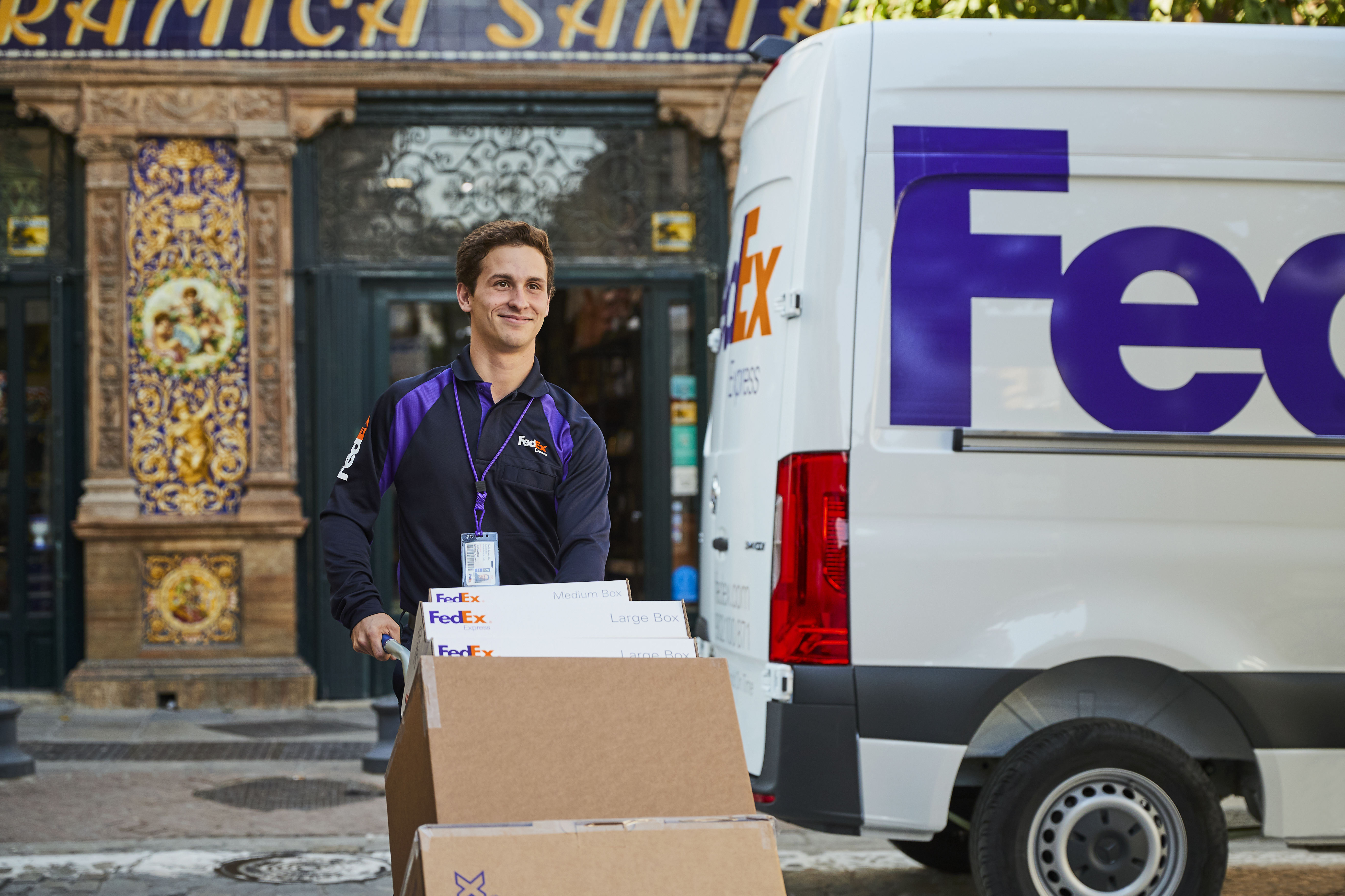 Een glimlachende FedEx-koerier loopt weg van een FedEx-bestelwagen met dozen