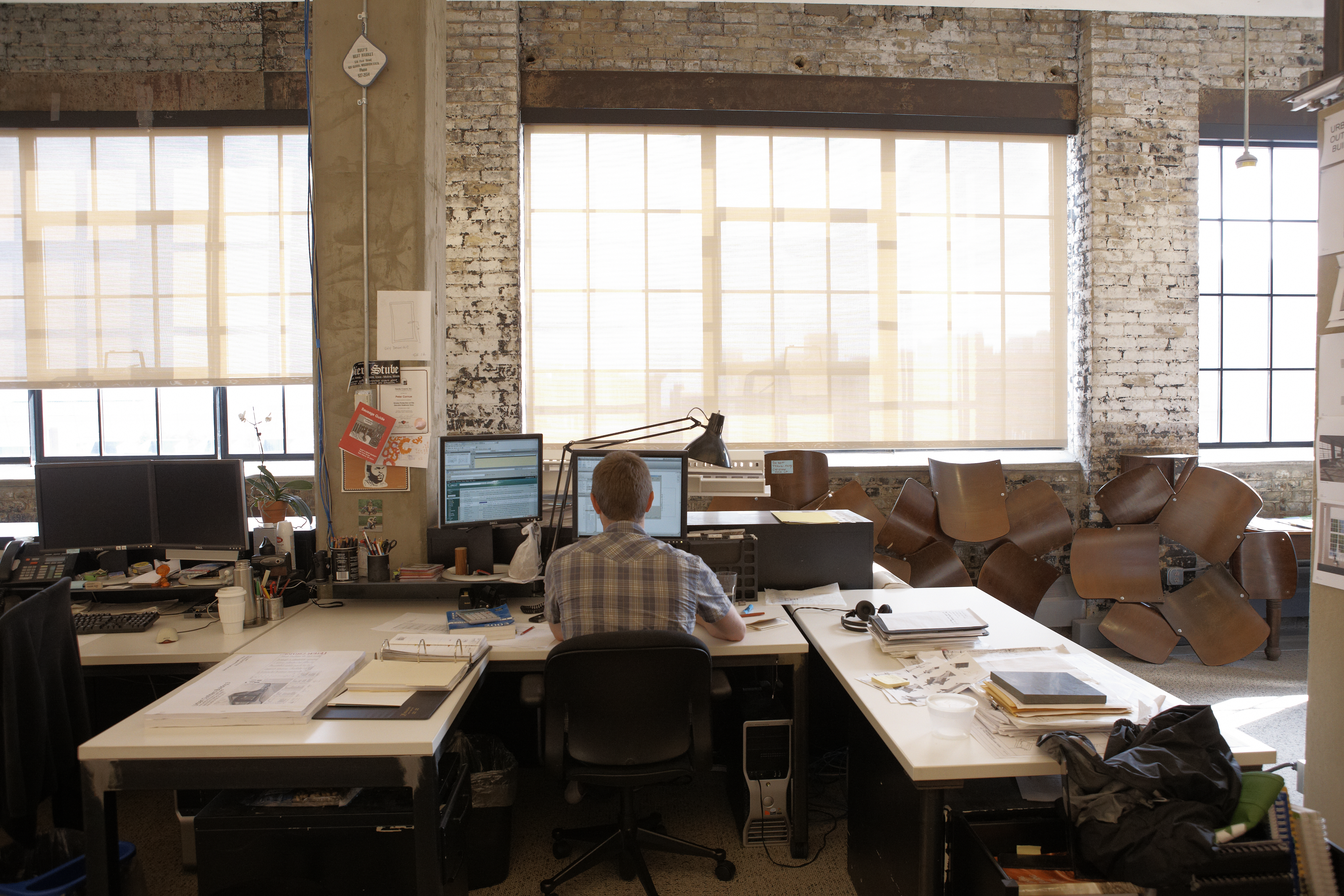 A man sits in a high-ceilinged brick and wood office facing his desktop computer