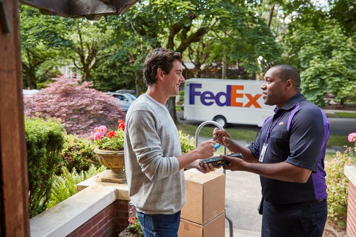 Courier delivering packages to man at home with FedEx Ground truck in background