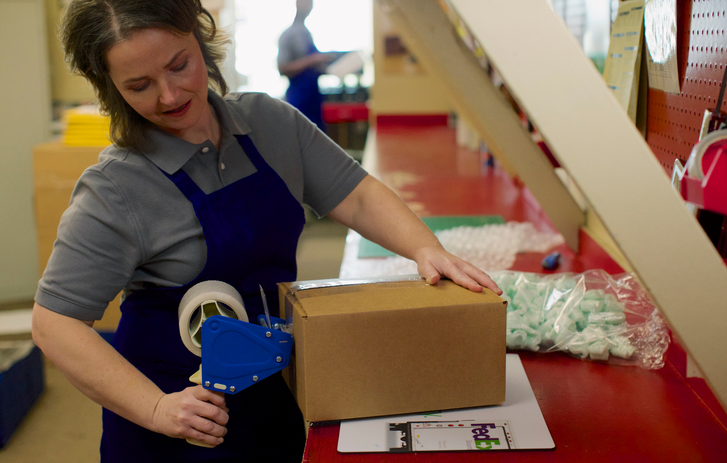Person verschließt ein Paket, Verpackungsmaterial liegt drumherum
