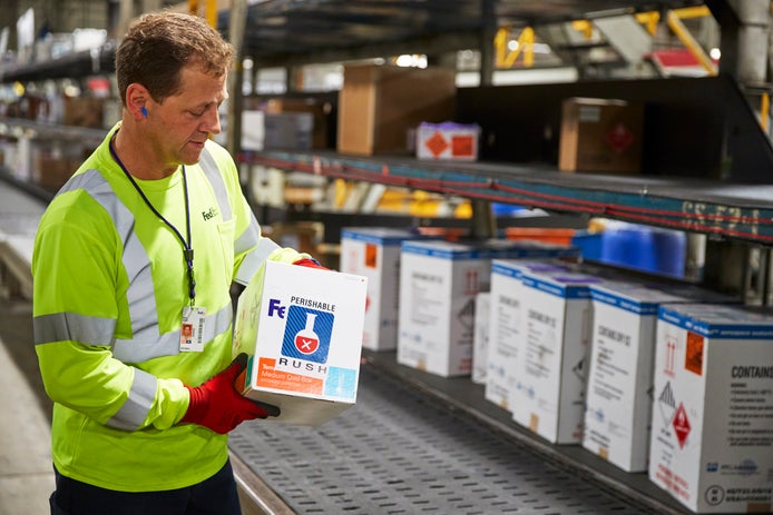 Lavoratore FedEx che mette una scatola su un nastro trasportatore