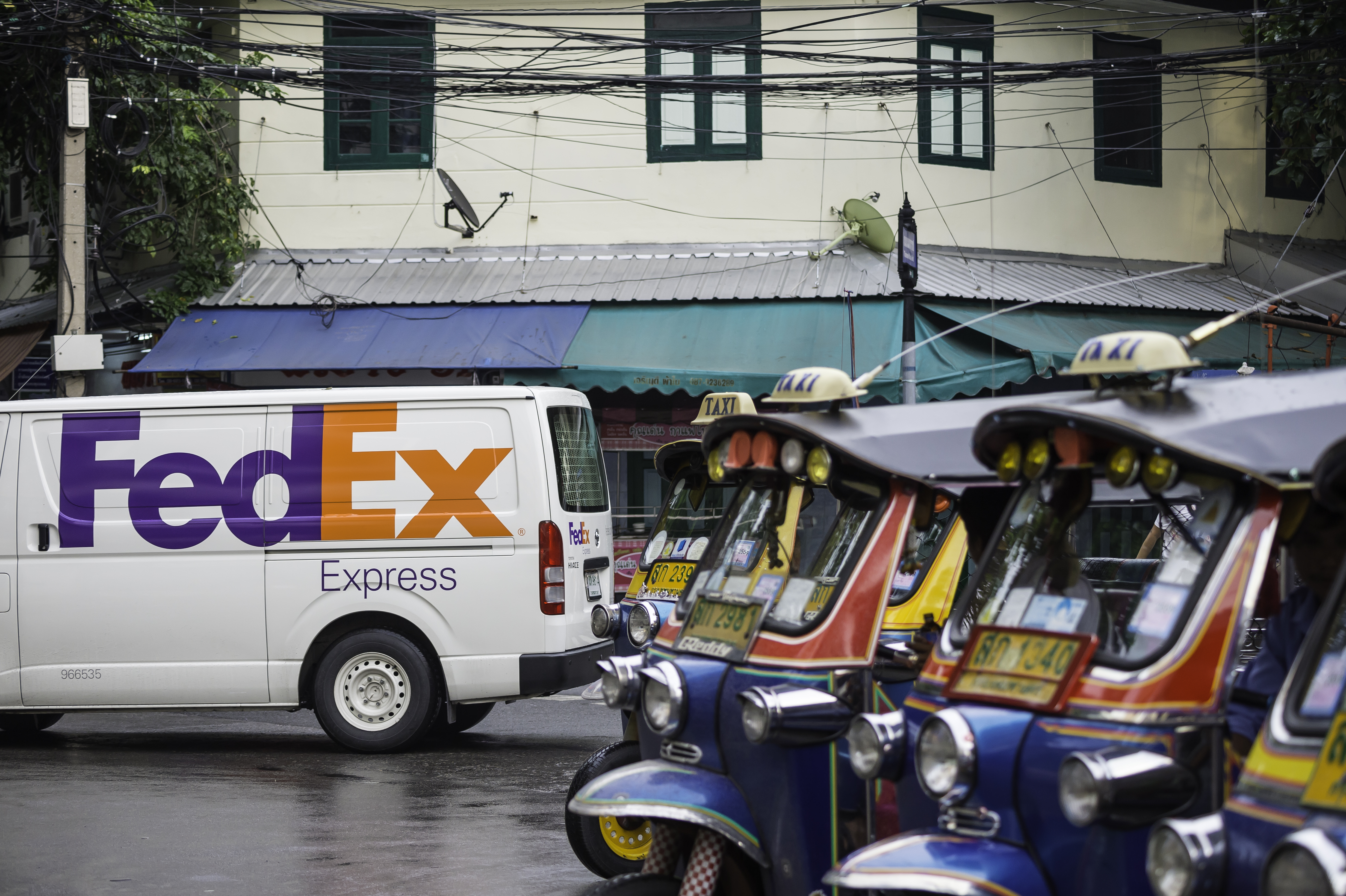 FedEx Express van on street with a line of mini taxis