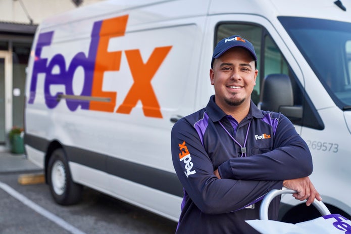 Un mensajero de FedEx orgulloso delante de una camioneta de FedEx Express