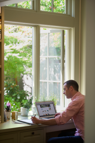 man writing on notepad next to laptop overlooking open window