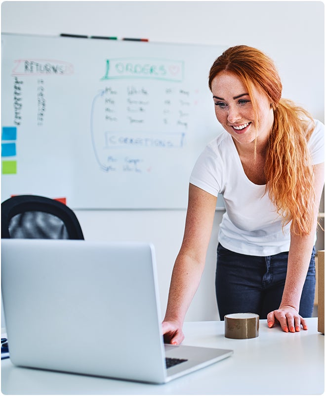 a woman stands in front of a whiteboard and uses a laptop computer on the table