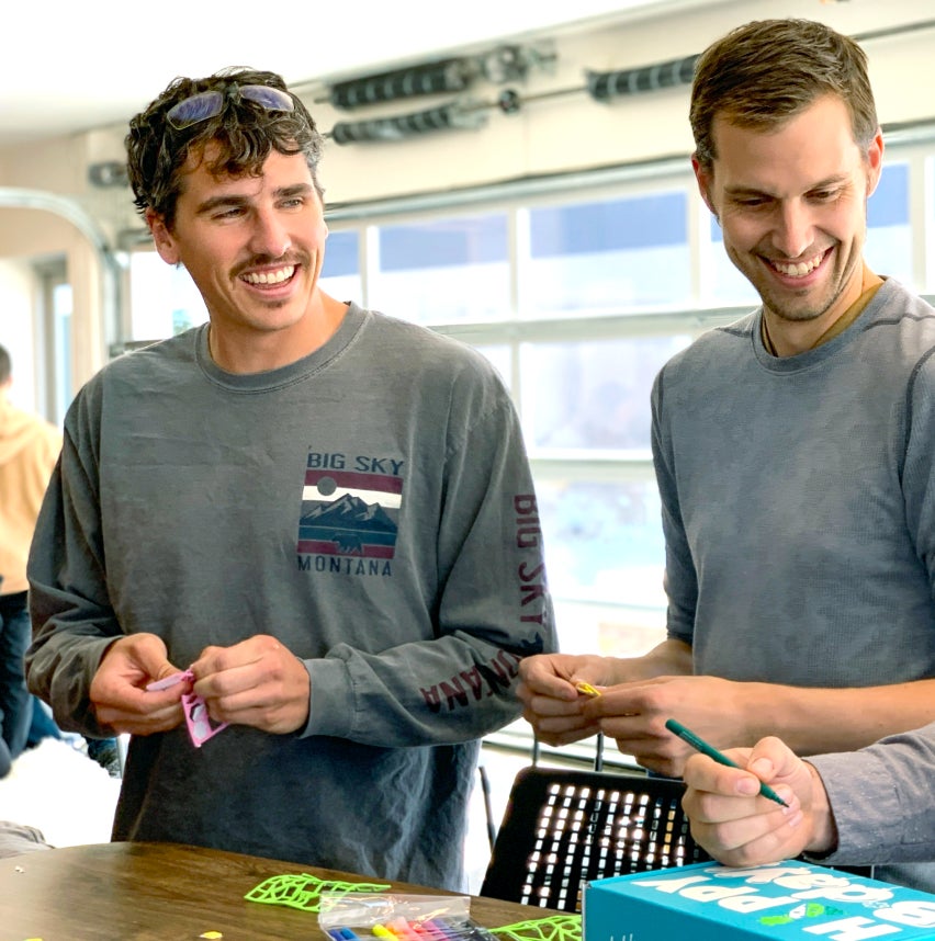 Two men smile while standing at a table helping to decorate a Birthday Box