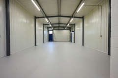 The interior of a warehouse unit, facing the front electric roller shutter, which is closed and large enough for vehicle access.