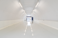 An empty arch with white lining, facing the front electric roller shutter entrance, which is closed. There is a WC cubicle at the front of the arch.