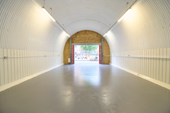 An empty arch with white lining, facing the front electric roller shutter entrance, which is open.