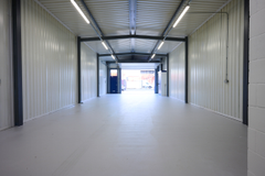 The interior of a warehouse unit, facing the front electric roller shutter, which is open and large enough for vehicle access.