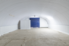 An empty arch with white lining, facing the front electric roller shutter entrance, which is closed. There is a WC cubicle at the front of the arch.