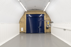 An empty arch with white lining, facing the front electric roller shutter entrance, which is closed.