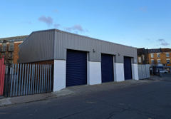 The front of a warehouse unit, with a closed electric roller shutter entrance big enough for vehicle access, and a pedestrian door.