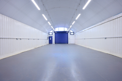 An empty arch with white lining, facing the front electric roller shutter entrance, which is closed.