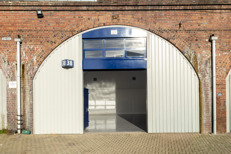 The front of an arch, with high level glazing, and an open electric roller shutter entrance big enough for vehicle access.