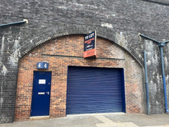 The front of an arch with a closed electric roller shutter entrance big enough for vehicle access, and separate pedestrian door.

