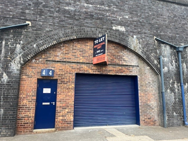 The front of an arch with a closed electric roller shutter entrance big enough for vehicle access, and separate pedestrian door.

