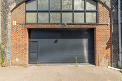 The front of an arch, with high level glazing, and a closed electric roller shutter entrance big enough for vehicle access.