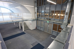 An arch with lining and a ground floor level and a mezzanine level, connected by stairs.