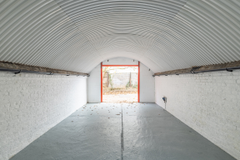 An empty arch with white lining, facing the front electric roller shutter entrance, which is open.