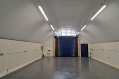 An empty arch with white lining, facing the front electric roller shutter entrance, which is closed.