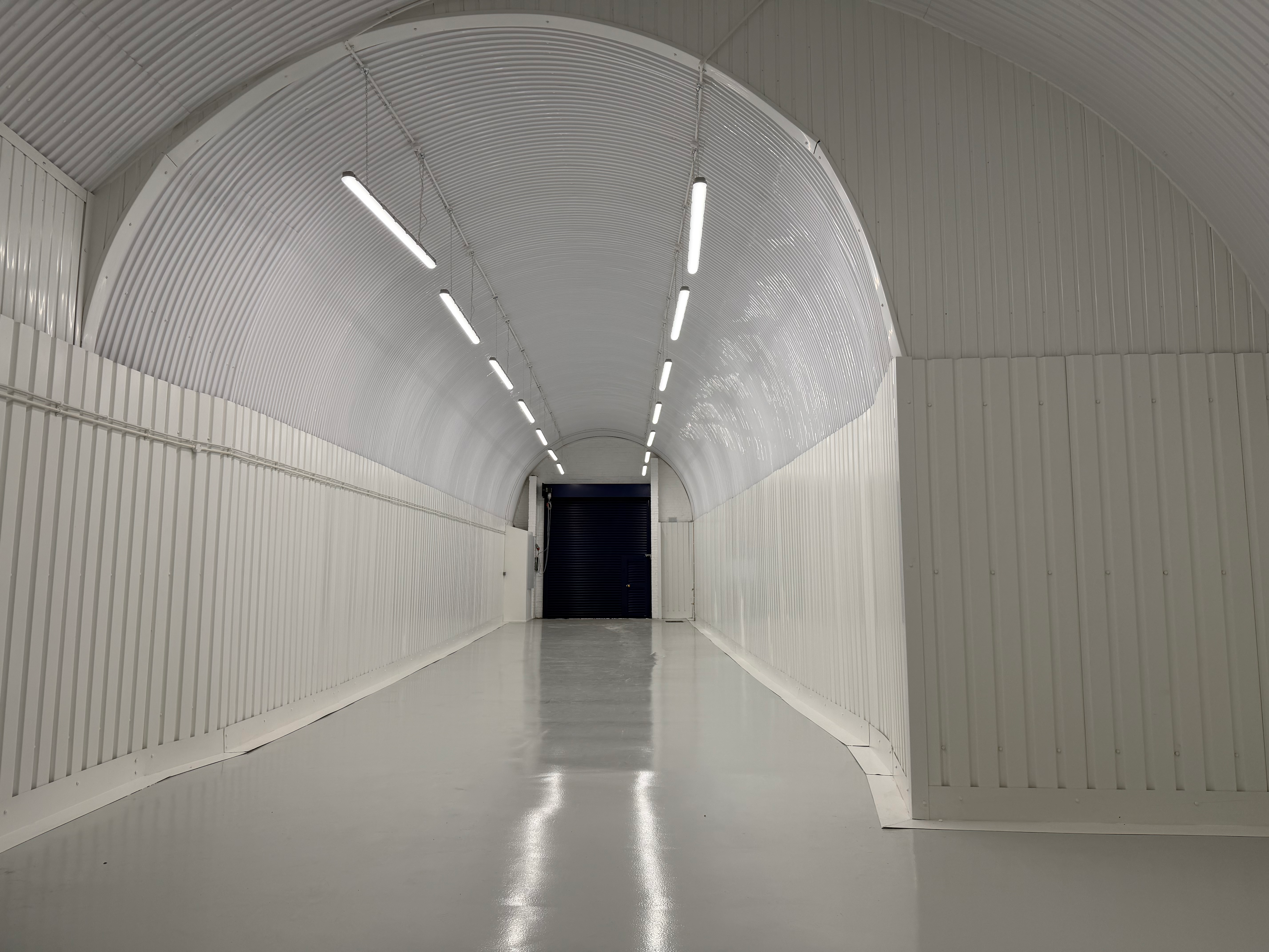 An empty arch with white lining, facing the front electric roller shutter entrance, which is open.