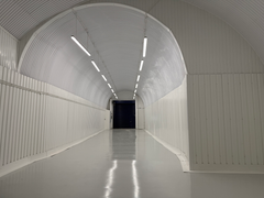 An empty arch with white lining, facing the front electric roller shutter entrance, which is open.