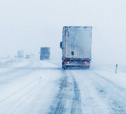 Freight trucks driving on a snowy highway in low visibility.