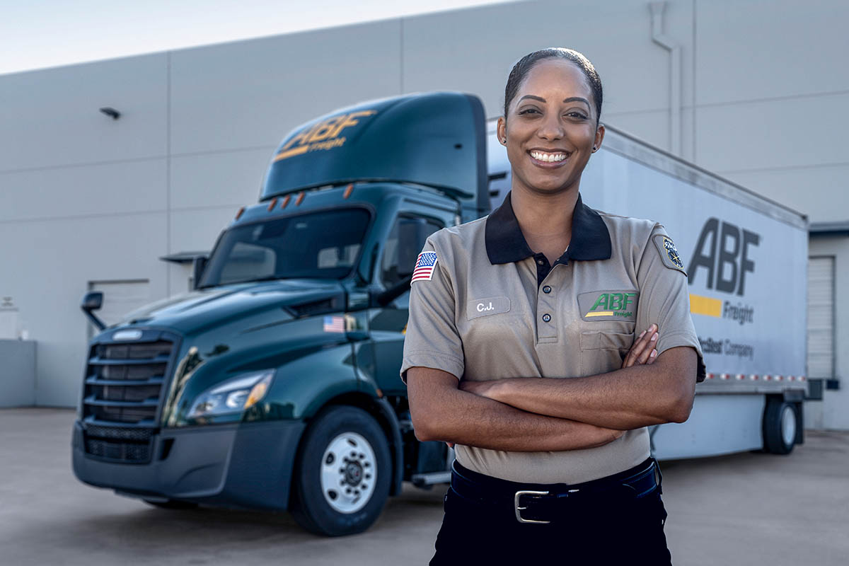 Female ABF Freight driver stands beside ABF truck.