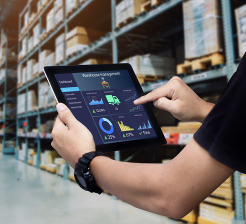 Employee using a tablet to monitor warehouse management data in a large storage facility.