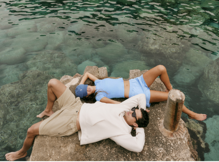 Vuori models lounging on a rock wearing versatile Vuori clothing and accessories