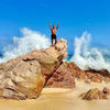 khalil rafati stands triumphantly atop a large boulder as wave crashes behind