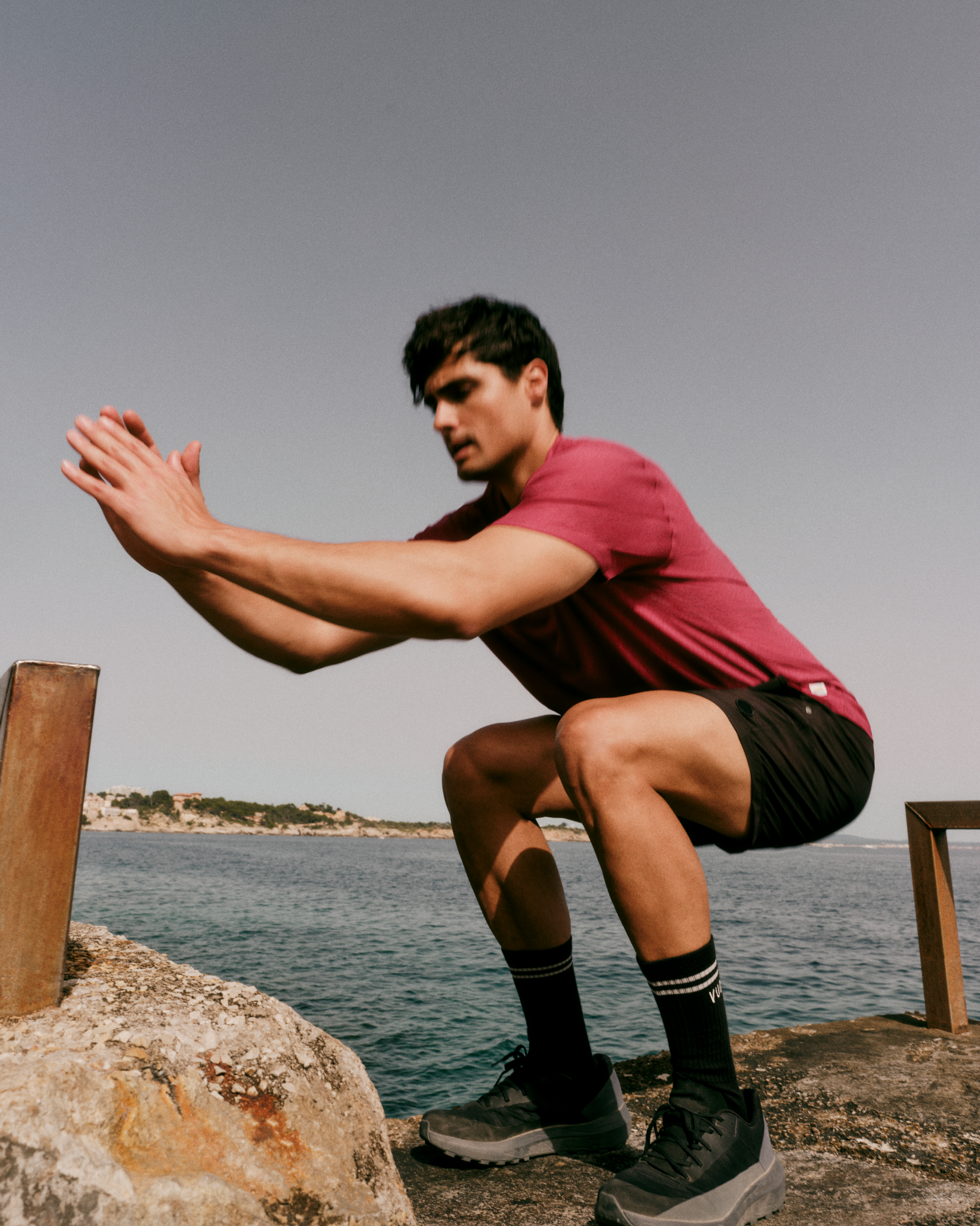 man wearing vuori doing squats by the ocean
