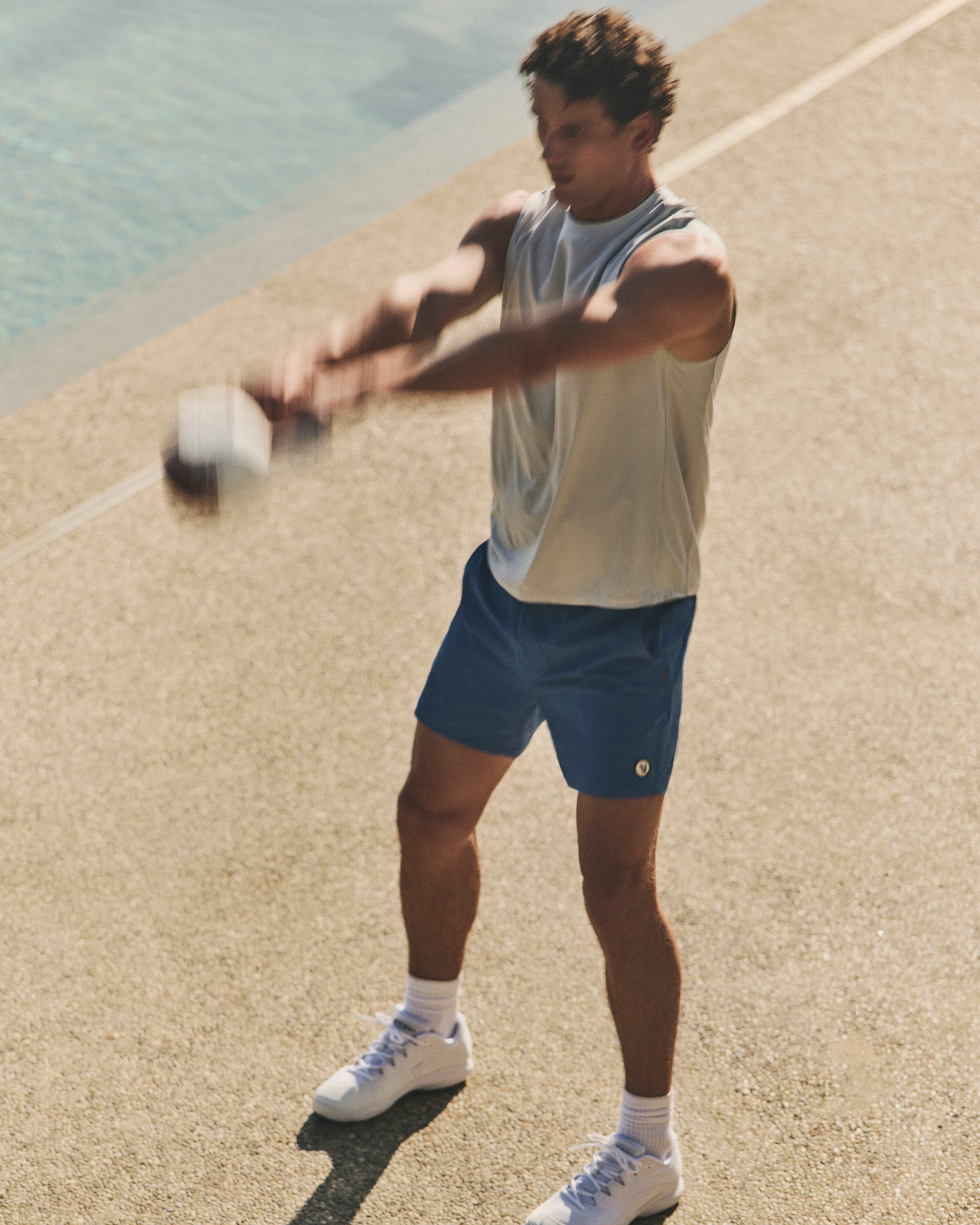 man wearing vuori swinging a kettlebell by the water 