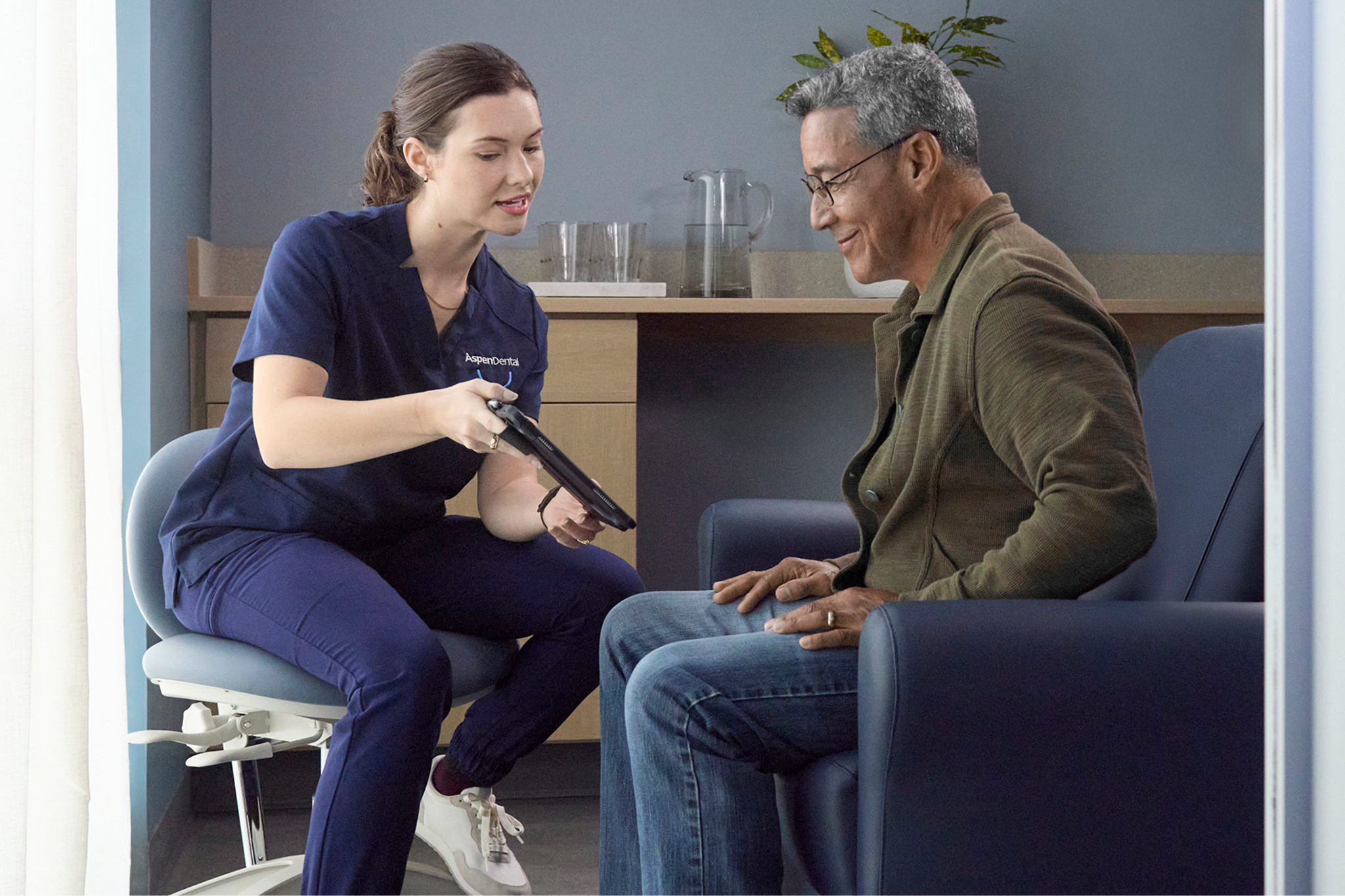 Aspen Dental team member showing a patient dental treatment information on a tablet during a consultation.