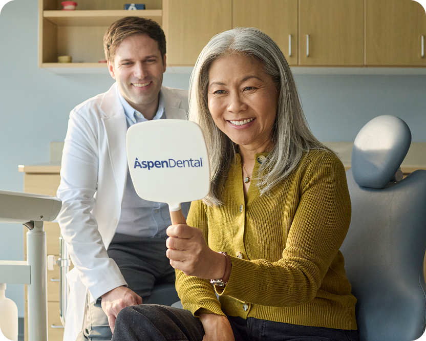 Alt text:
Patient smiling while looking at her teeth in an Aspen Dental mirror.